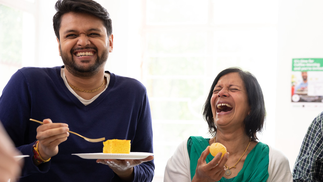 Three people are standing up and holding plates with different treats on them. Two people appear to be laughing. They look like they are inside a building. 