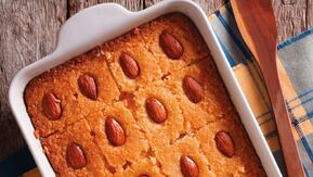 A golden tray of basbousa—soft, buttery semolina cake soaked in fragrant rose and lemon syrup—topped with whole almonds. Its rich, nutty texture and syrupy sweetness make every bite irresistible.