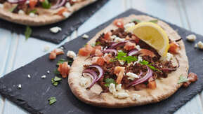 Two lahmacuns are each placed on rectangular slate plates. They are topped with different vegetables and cooked minced meat. 