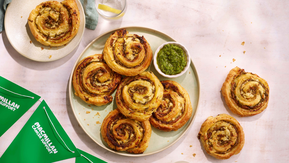 A plate of round pastry pinwheels and a small bowl of green pesto.