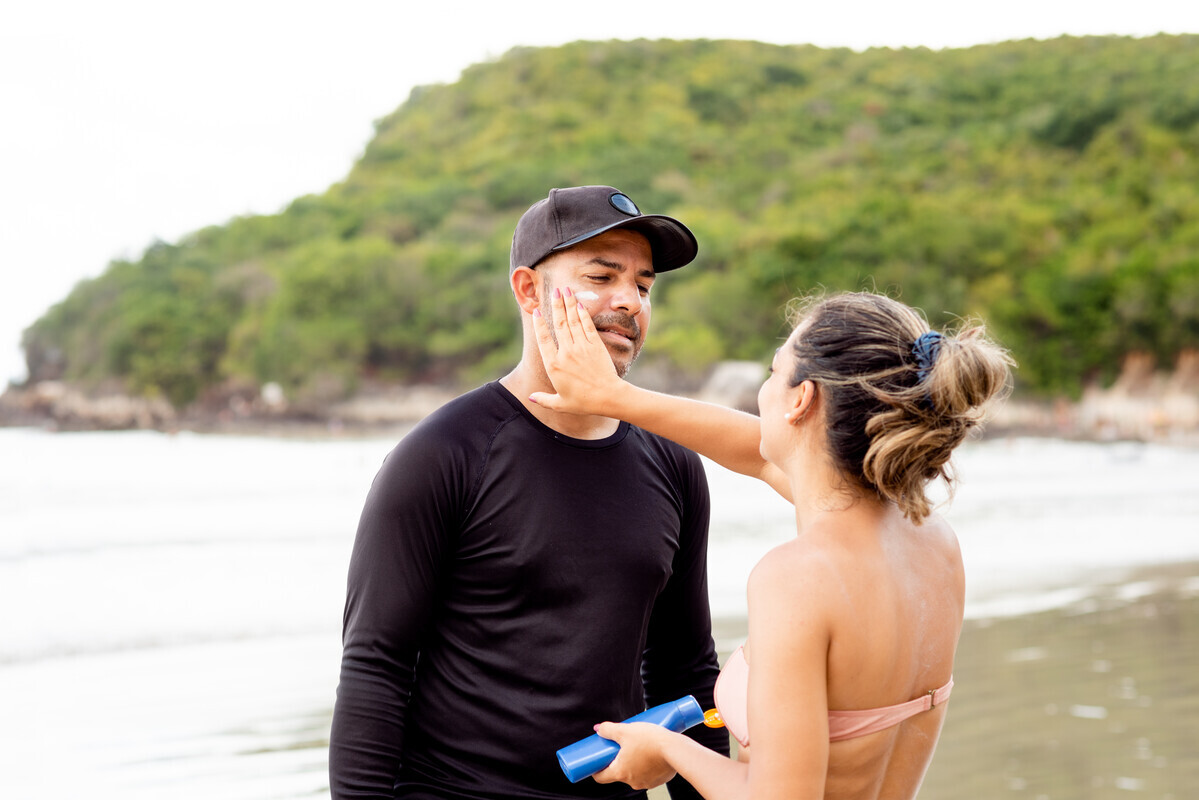 Woman applying sunscreen to mans face while at a beach.