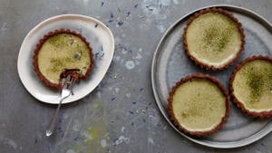 There is plate with three tarts on it. There is also a smaller plate with a tart on it that has a bite missing from it and a fork on it. The tarts have a red base. 