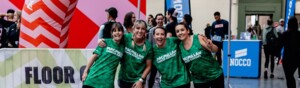 A group of 4 people are standing side by side. They are all wearing Macmillan branded tops. They appear to be inside a building at an event. 