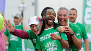 Three smiling men in team Macmillan shirts pose for a picture at a fundraising event.