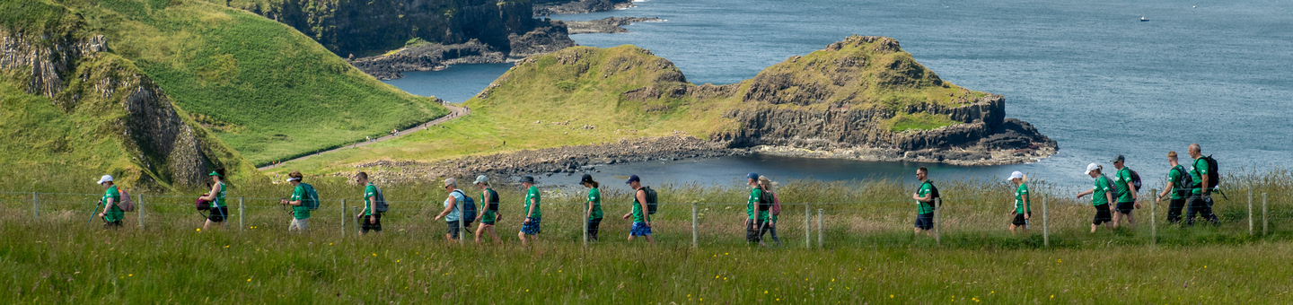 A line of Mighty Hikers walking across a path with the sea in the background