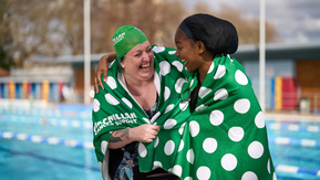 Two women in green spotty towels laughing together next to an outdoor pool