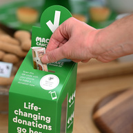 Someone placing money into a green Macmillan donation box.