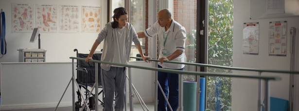 A nurse helping a patient to walk through parallel rails