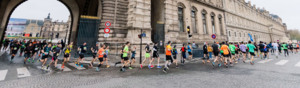 Many runners are running from under an archway and on to a street in Paris. They are taking part in the Paris marathon.