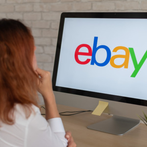 A person is leaning on a desk and looking at a computer. The screen has the eBay logo on it.