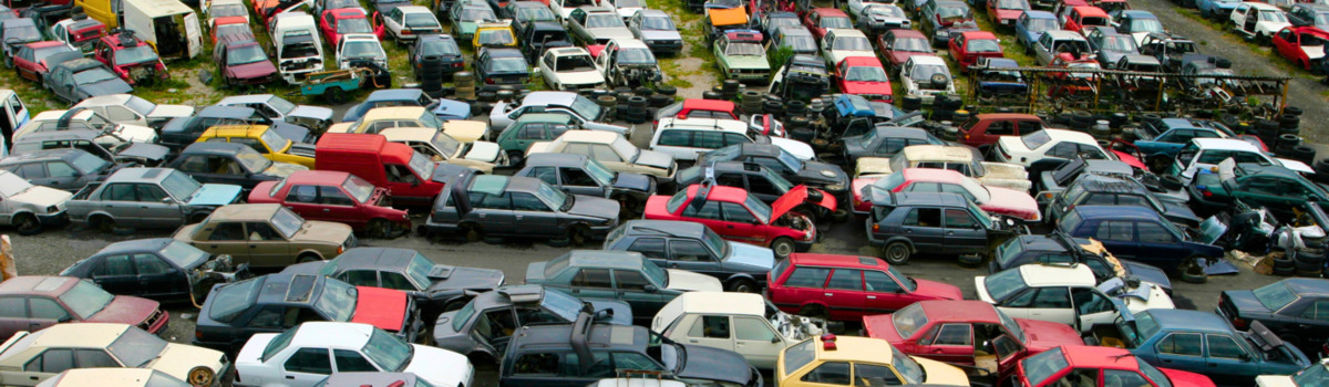 Many cars are parked in a scrap yard. Some of the cars appear to be damaged. 