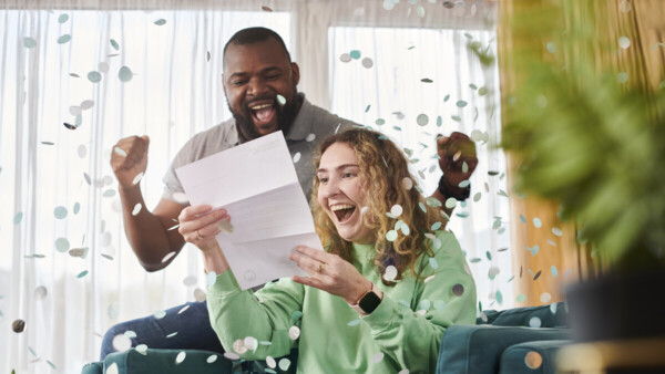 Two people are looking really excited as they read a letter. There is confetti falling around them.