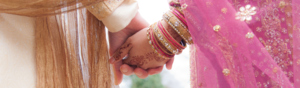 A close view of a couple holding hands. They are in traditional Indian wedding attire.
