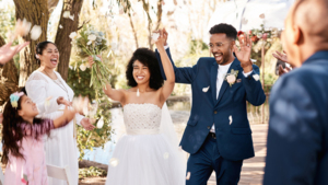 A bride and a groom are walking down the aisle celebrating. The bride is holding a bouquet in the air. People are celebrating on either side of the pair. They are outside.