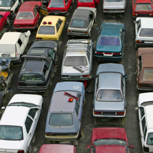 Many cars are parked in rows in a car scrap yard. The cars appear to be damaged. 