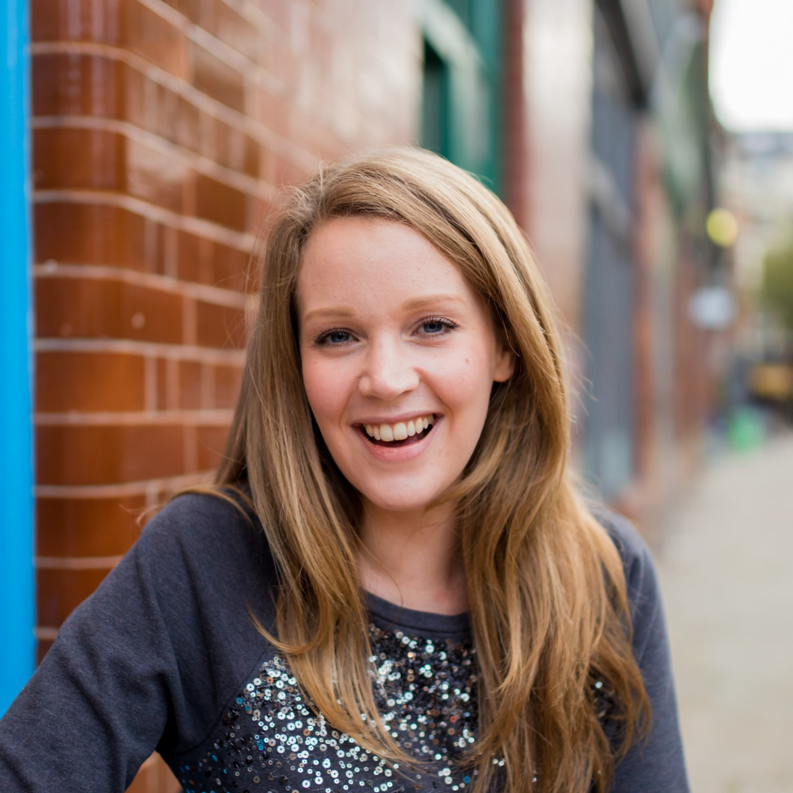 Photo of Yvonne. She is standing in front of a brick wall, looking at the camera and smiling.