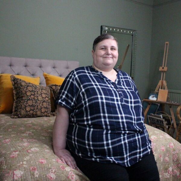 Sarah is sitting on a bed, looking at the camera and smiling.