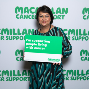 A south Asian lady with brown hair with a sign supporting people with cancer .