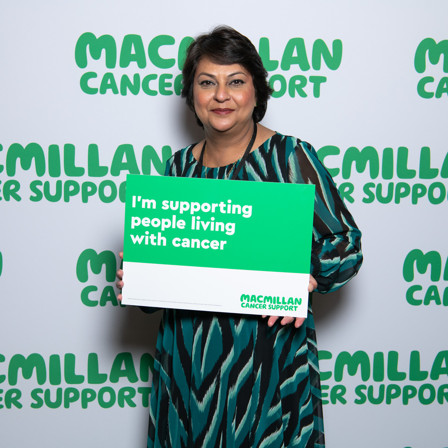 A south Asian lady with brown hair with a sign supporting people with cancer .