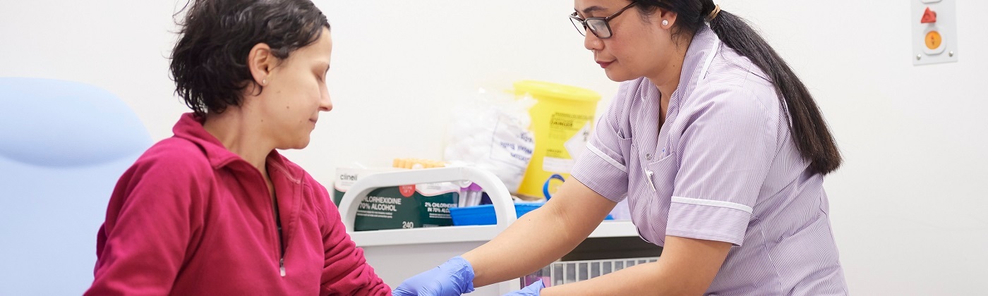 A nurse with long hair and glasses is treating a female patient with short hair.