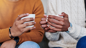 A photo close-up of two pairs of hands, both holding a mug.