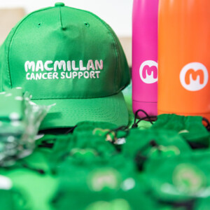 A table of Macmillan branded merchandise including caps, metal water bottles, and folded t-shirts.
