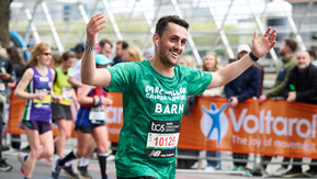 A man running the London Marathon holding both hands up in the air to get cheers.