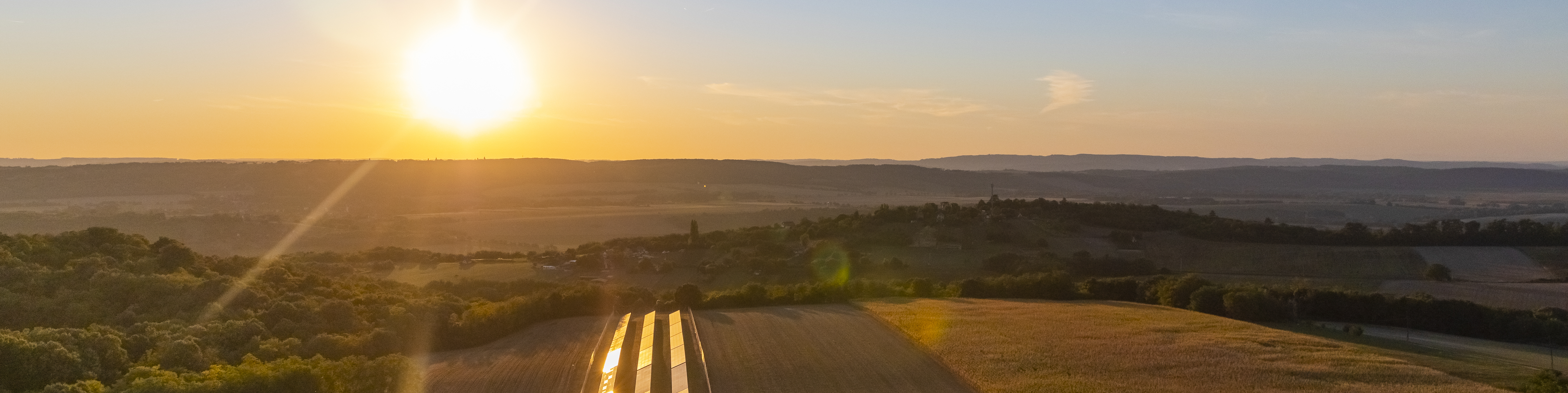 An aerial view solar panels near a farm and agricultural fields as the sun rises.