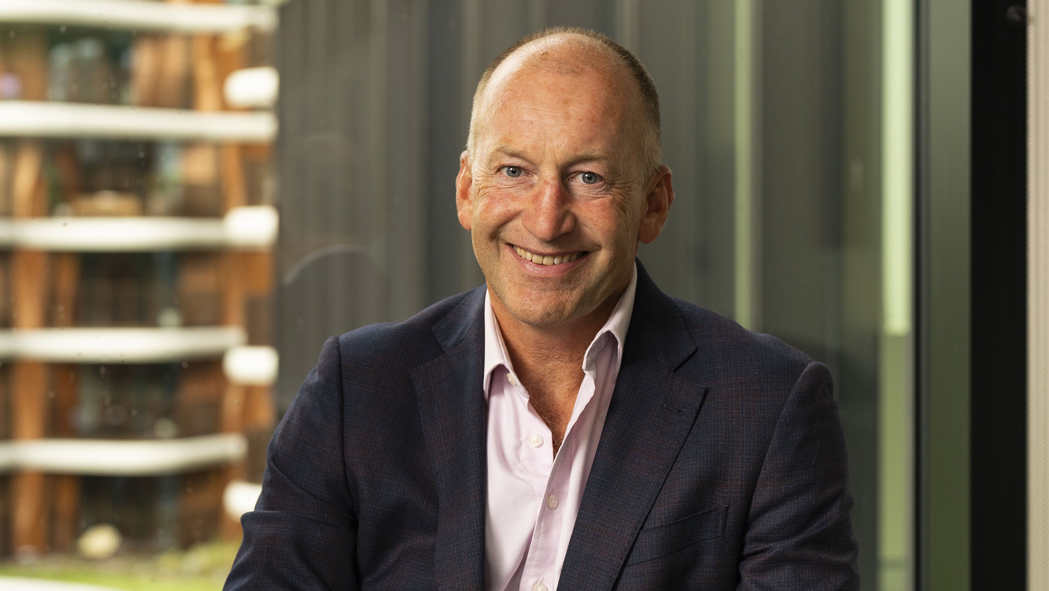 Photograph of David. He is wearing a suit, while sitting in a green chair, and smiling at the camera.