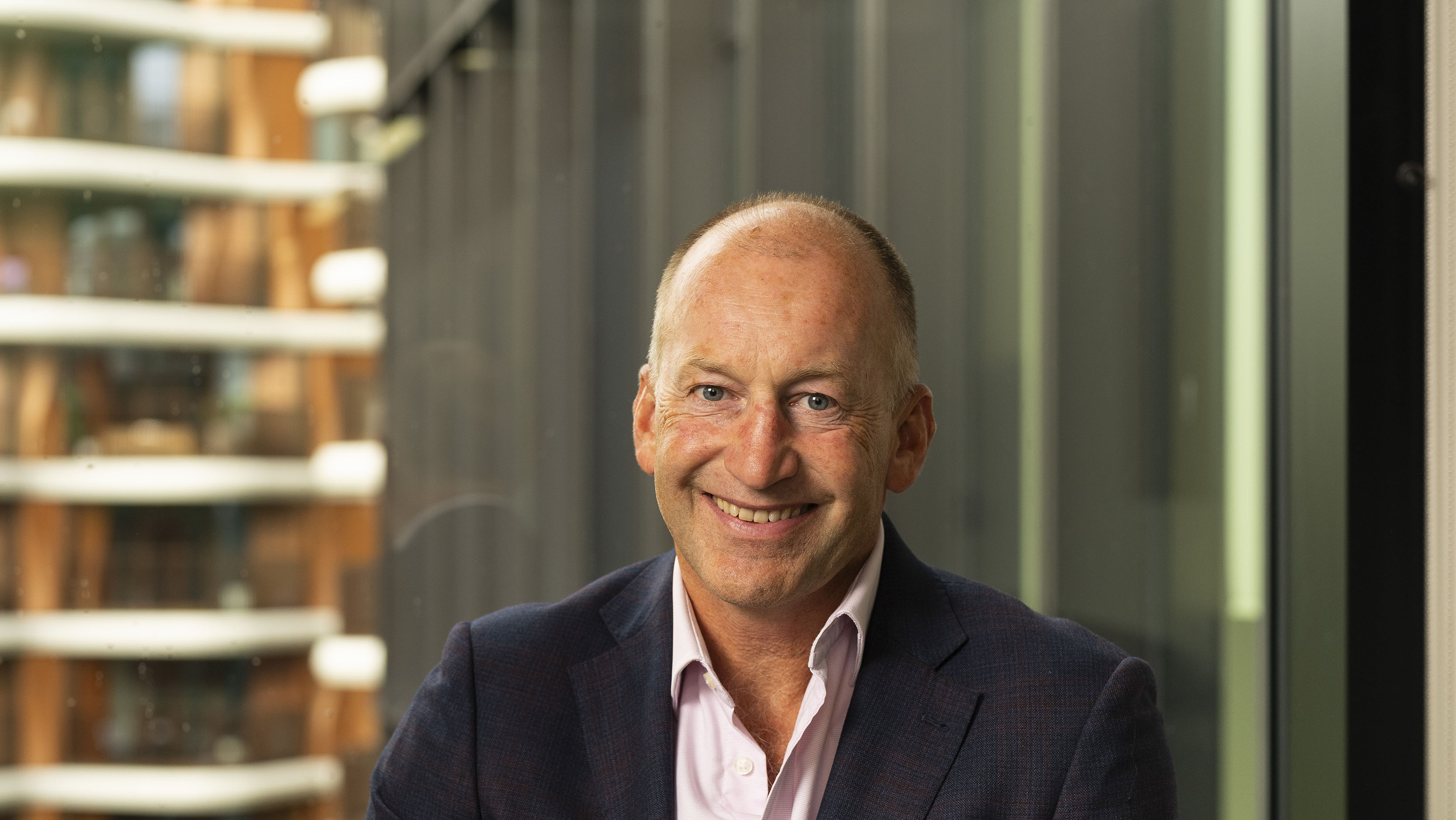 Photograph of David. He is wearing a suit, while sitting in a green chair, and smiling at the camera.