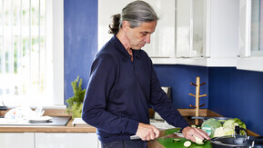 Man standing in kitchen chopping vegetables
