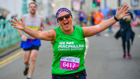 A woman wearing a headband and a green Macmillan running t-shirt with her arms spread and smiling