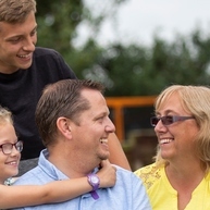 A man and woman sitting in the garden with their two children, a boy standing behind them and a girl with her arms around the man