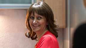 Woman in red top smiling while standing in a kitchen.