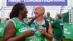 A group of Mighty Hikes participants are celebrating after finishing after a hike. They are holding glasses of fizz and in a side hug. Behind them is a sign that reads finish - congratulations.