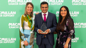 Three people are posing for a photo at an event. The person in the middle is holding a glass trophy. 