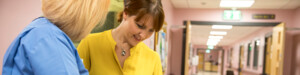 Two healthcare professionals looking through documents. They are standing in a hospital hallway