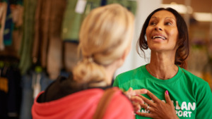 A Macmillan volunteer and another person are speaking to each other. The volunteer is wearing a green Macmillan top. 
