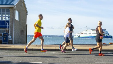 Runners are running on path near the sea. The path is paved. They appear to be competing in a running event.