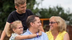 A man and woman sitting in the garden with their two children, a boy standing behind them and a girl with her arms around the man
