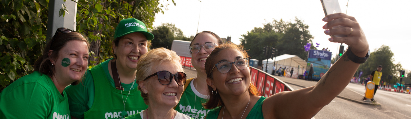 A group of volunteers are taking a selfie. They are wearing green tops with the Macmillan logo on them. They appear to be at an outdoor event. 