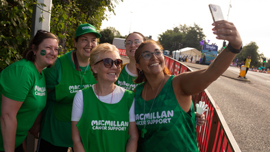 A group of volunteers are taking a selfie. They are wearing green tops with the Macmillan logo on them. They appear to be at an outdoor event. 