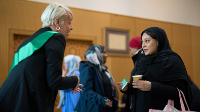 A woman talking and handing out Macmillan information to another woman at a Coffee Morning