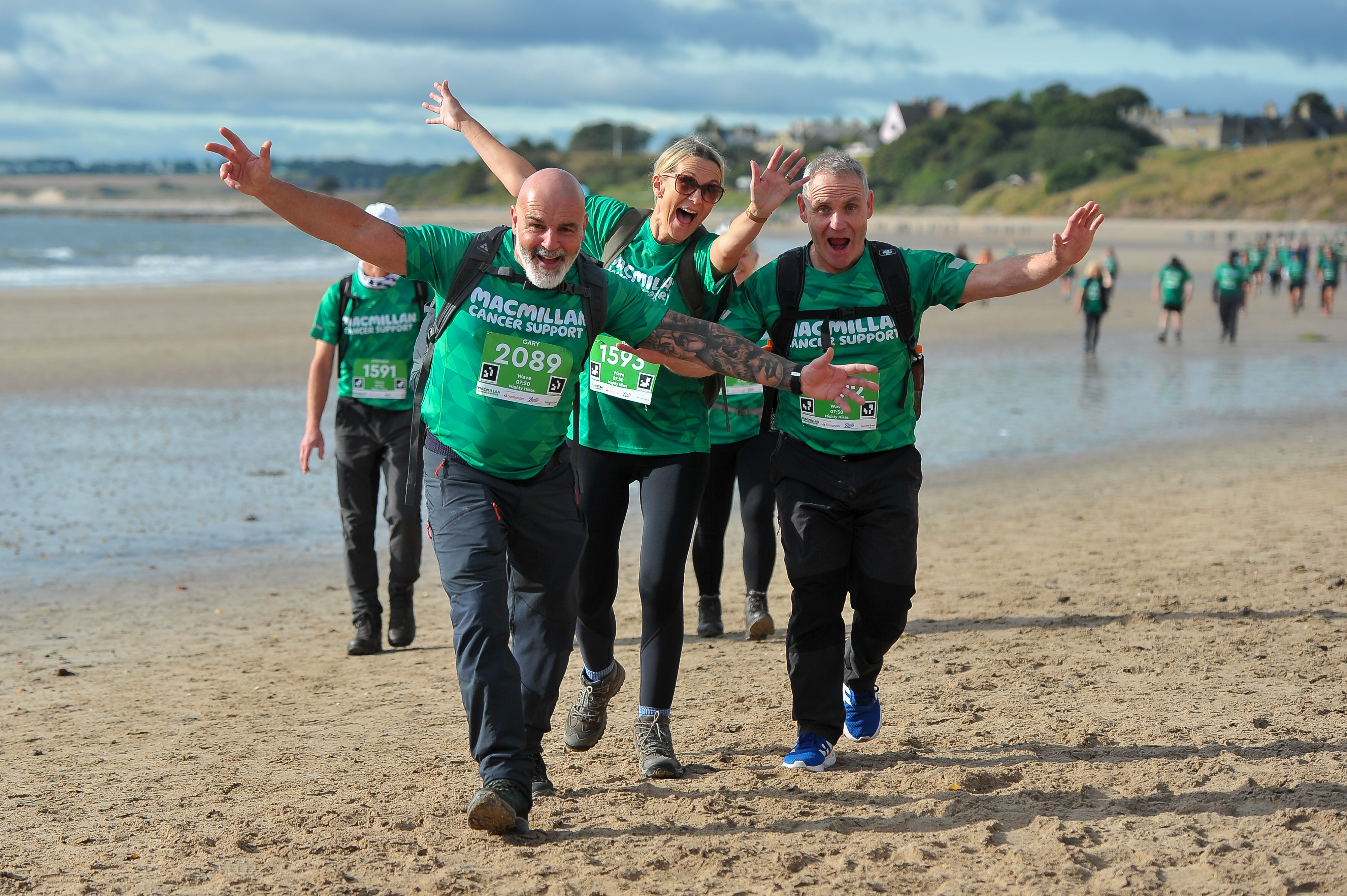 People walking along a beach waving at the camera