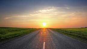 A sunrise over a road with fields either side.