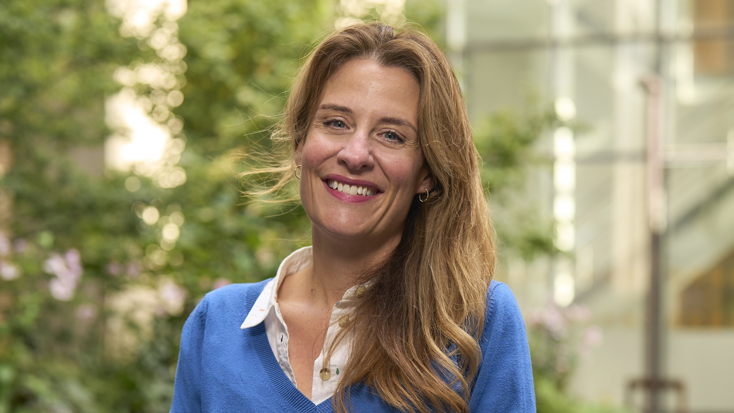 Gemma Peters with long brown hair, smiling at the camera in a blue outfit.