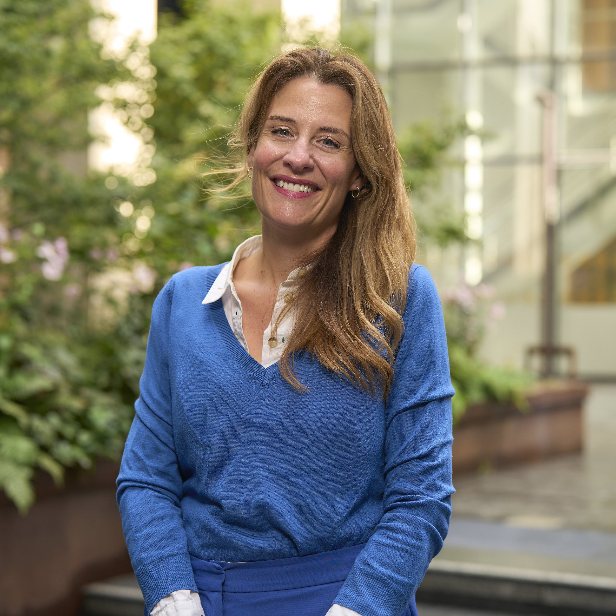 Gemma Peters with long brown hair, smiling at the camera in a blue outfit.