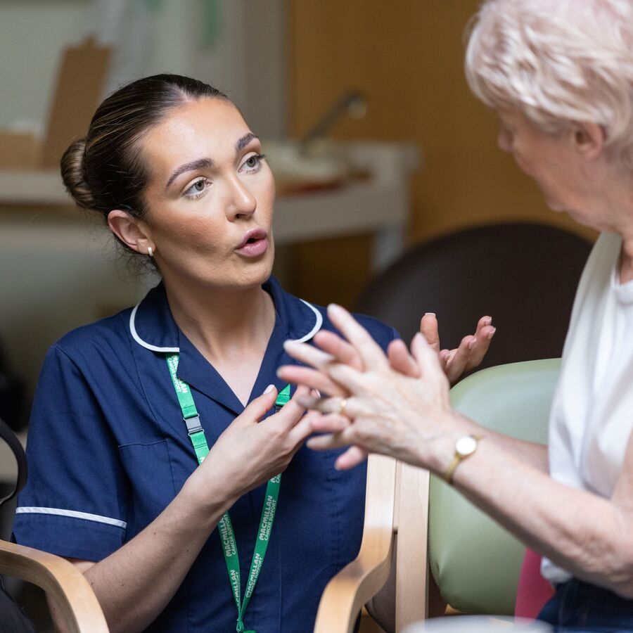 A Macmillan nurse is sitting between two patients in a group and is talking with one of them