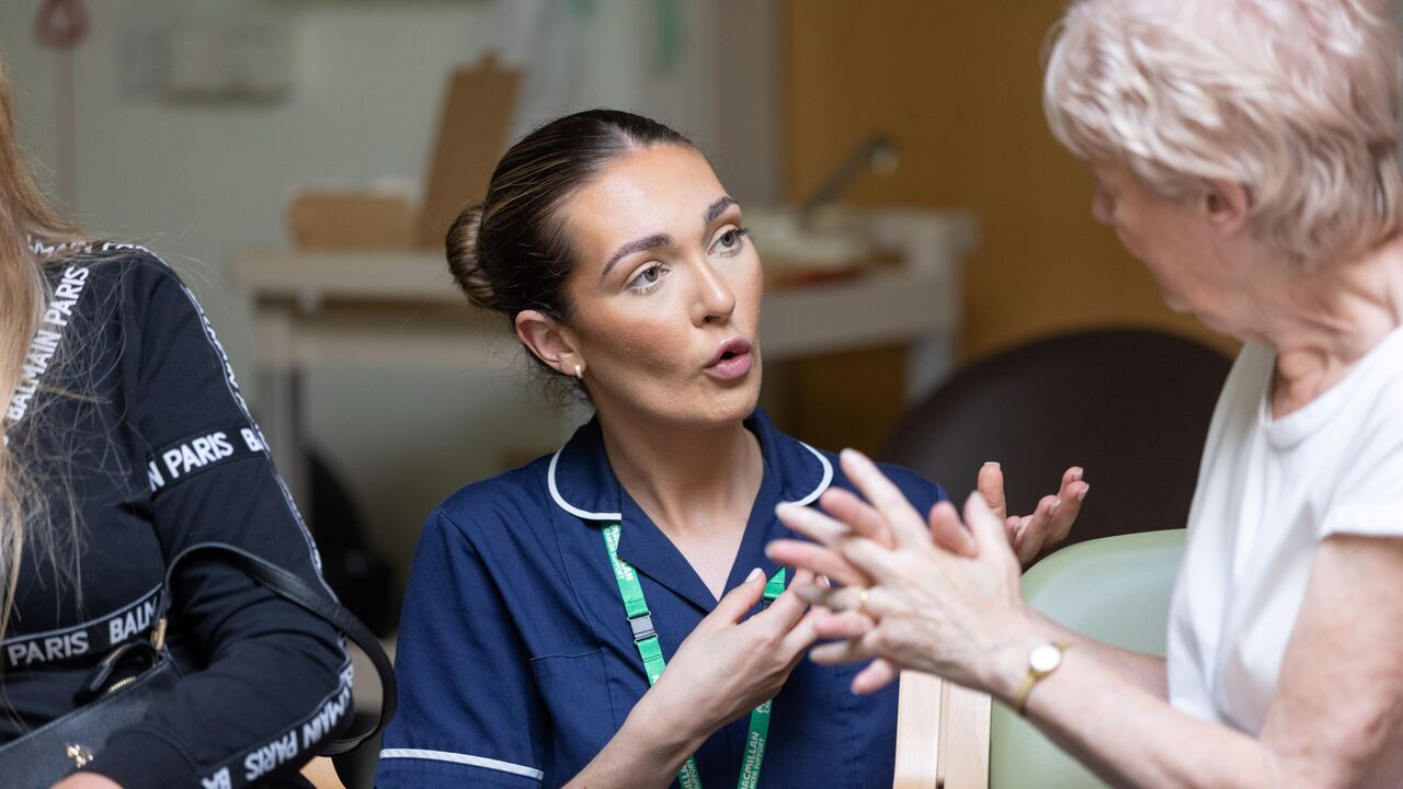 A Macmillan nurse is sitting between two patients in a group and is talking with one of them