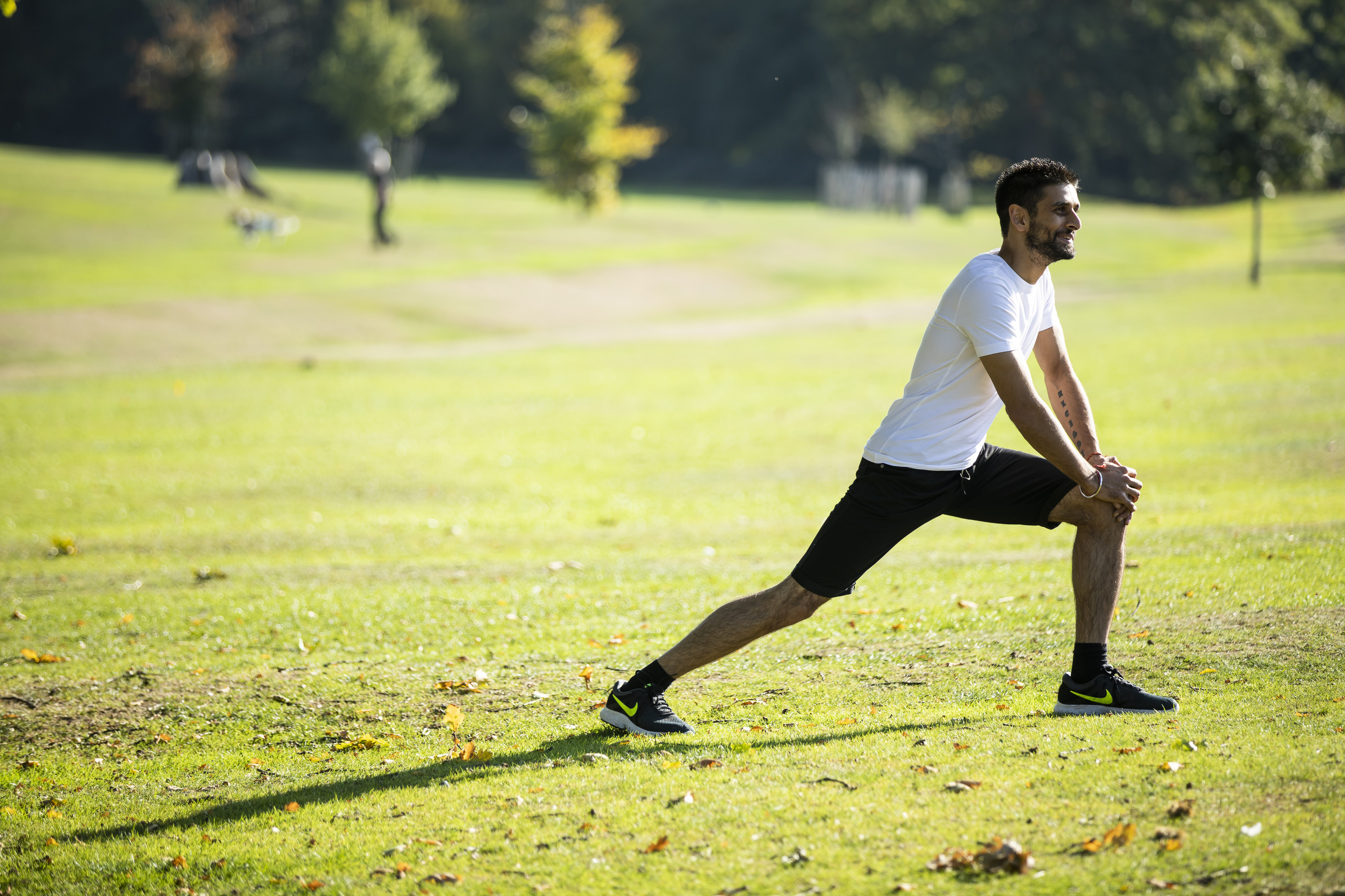 A man doing a stretching lunge in a park.